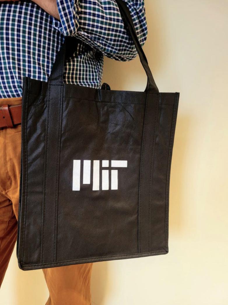 Person holding a black tote bag with a white MIT logo.